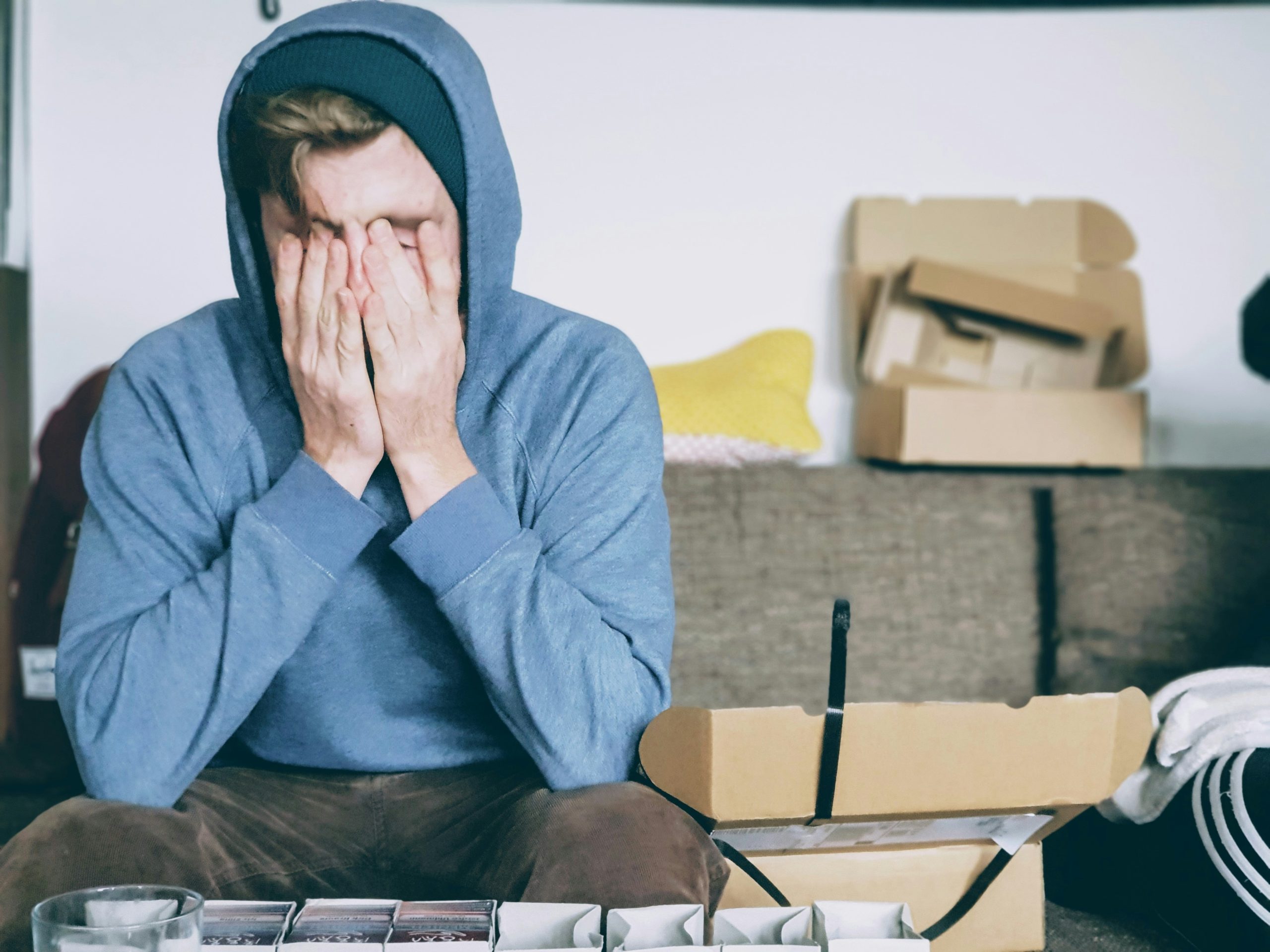 man in blue hoodie with hands on face