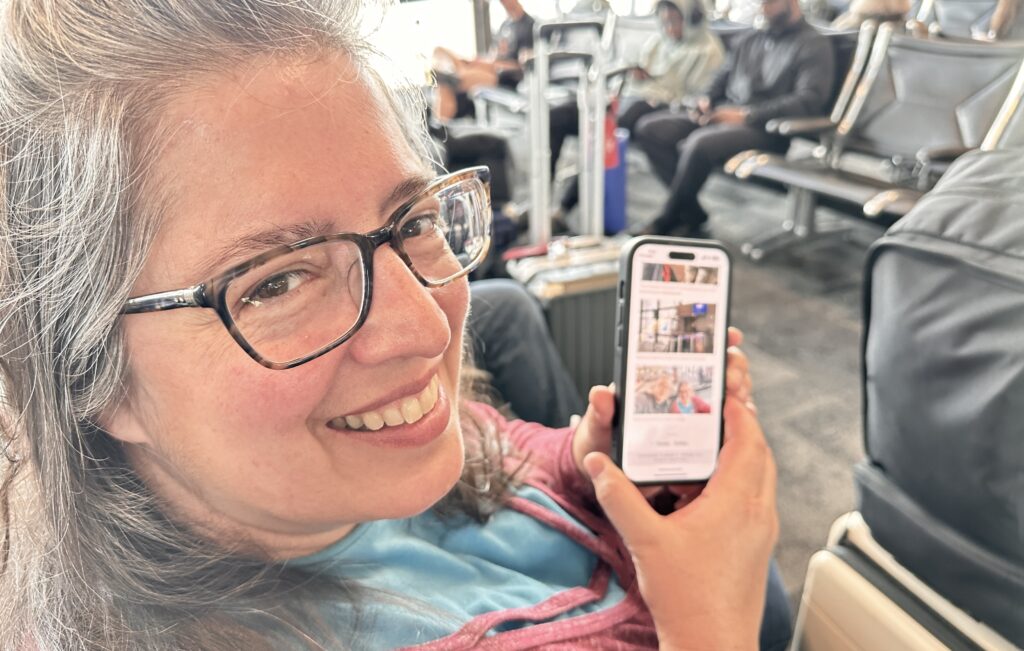 Ruhi smiling at the camera holding her phone which is viewing this website 