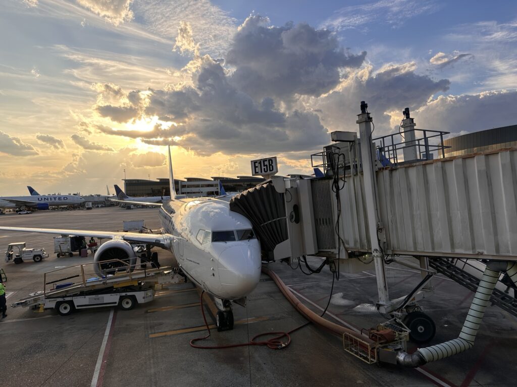 A plane attached to a gang plank with the sun setting behind it. 