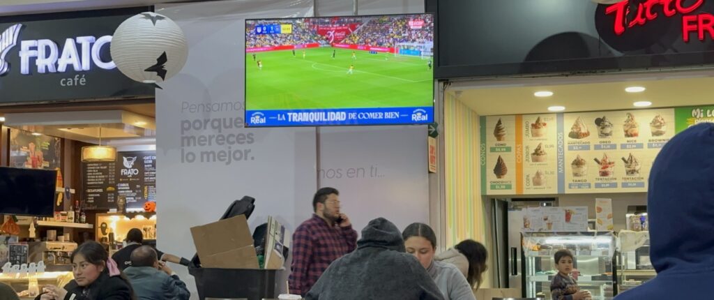 A soccer match on a TV screen in a food court