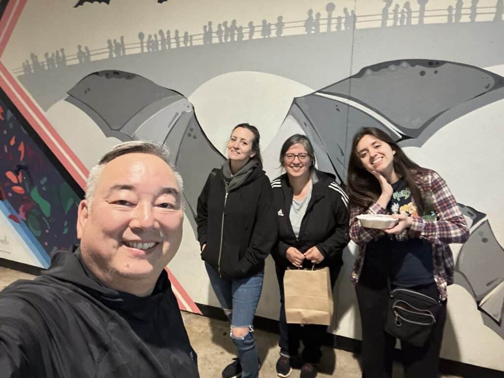 four people standing in front of a mural for a selfie